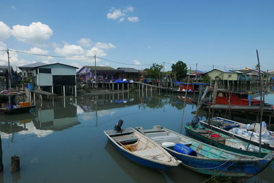 Boats moored in lake by houses against sky