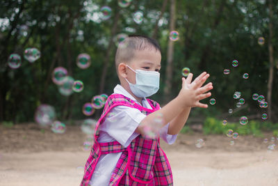 Boy wearing mask playing with soap bubbles standing outdoors