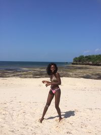 Full length of happy woman in bikini at beach against clear sky