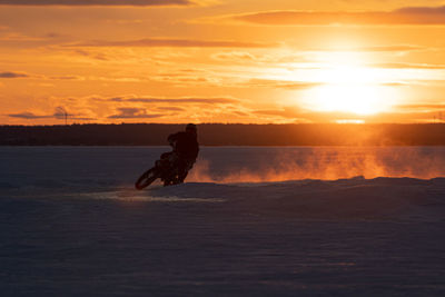 Motocrosso on frozen lake against sky during sunset