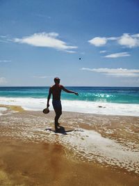 Shirtless young man standing at beach against sky