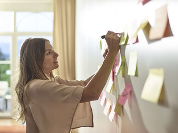 Woman writing on sticky note at the wall