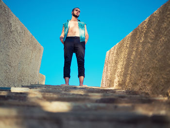 Low angle view of man standing on steps against clear blue sky