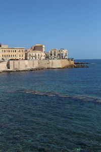 Buildings by sea against clear blue sky