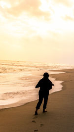 Rear view of silhouette man on beach against sky during sunset