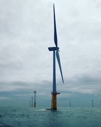 Traditional windmill by sea against sky