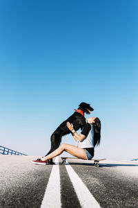 Woman with dog and skateboard against clear blue sky