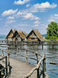 Wooden pier over lake by building against sky