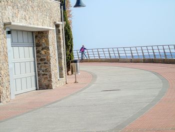 Man walking on footpath by building against sky