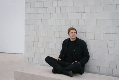 Portrait of young man sitting against wall