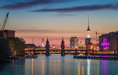 Illuminated city at waterfront during sunset