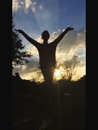 Silhouette of man with arms outstretched standing at sunset