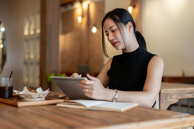 Young woman using mobile phone while sitting on table