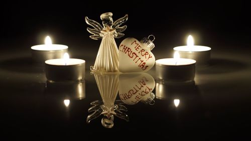 Heart shape pendant by angel figurine with burning christmas candles in darkroom