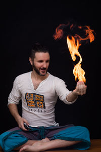 Young man sitting by fire against black background