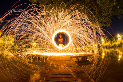 Man spinning wire wool on pier over lake at night