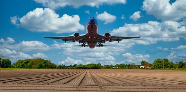 Airplane flying over agricultural field against sky