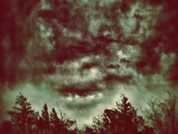 Low angle view of trees against cloudy sky