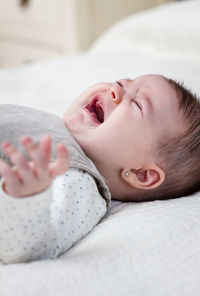 Cute baby girl crying while lying on bed at home