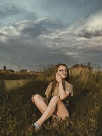 Portrait of woman sitting on field against sky