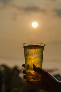Close-up of hand holding drink against sunset
