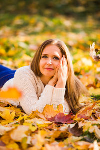 Portrait of young woman lying on leaves during autumn