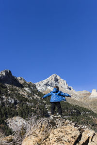 Boy standing on rock against clear blue sky