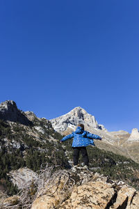 Man standing on rock against blue sky