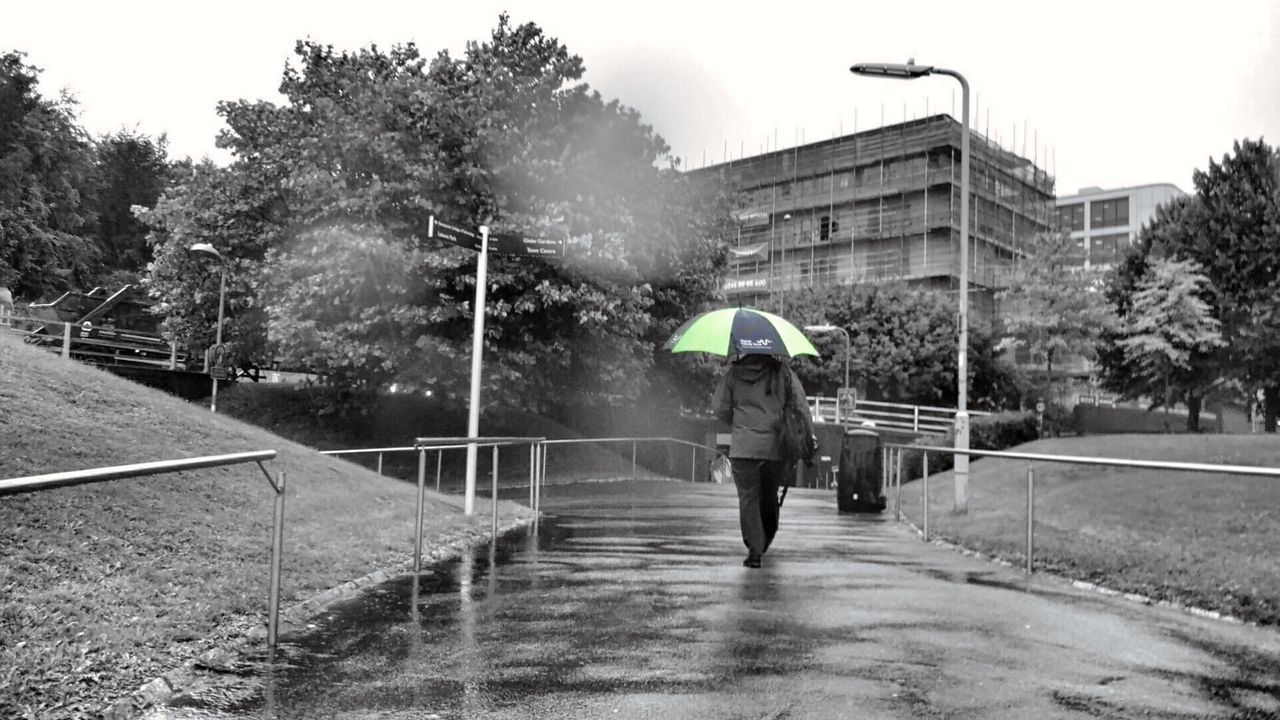 REAR VIEW OF MAN WALKING ON WET RAINY DAY