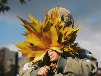 Child covering face with maple leaves
