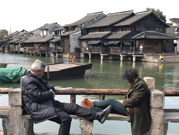 Men sitting by lake against built structure
