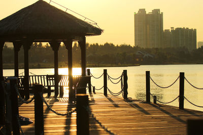 Wooden pier in city against sky during sunset