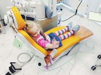 High angle view of girl waving hand while sitting on dentist chair