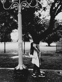 Full length of woman standing on footpath by tree