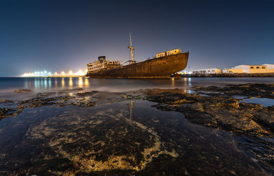 Abandoned boat on sea against clear sky at night
