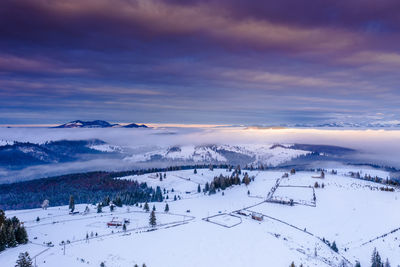 Snow covered landscape against sky during sunset