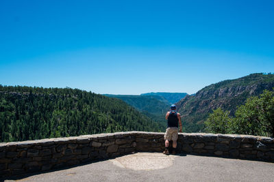 Rear view of man standing on mountain against clear blue sky