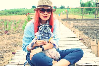 Portrait of woman with dog sitting on footbridge at agricultural field