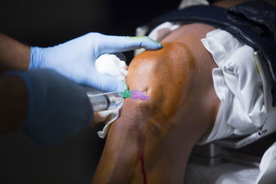 Cropped hands doctor injecting syringe patient knee 