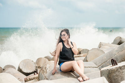 Young woman sitting on rock at beach against sky