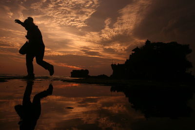 Reflection of silhouette woman on beach against sky during sunset