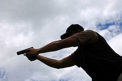 Low angle view of man shooting gun against sky