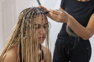 A stylist mother getting her teenage daughter senegalese braids in her home. 