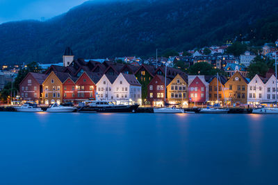 Buildings by lake against sky at dusk