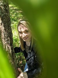 Portrait of smiling young woman against tree trunk