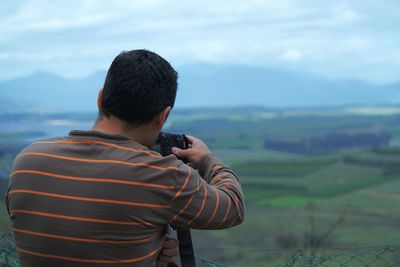 Rear view of man photographing landscape against sky