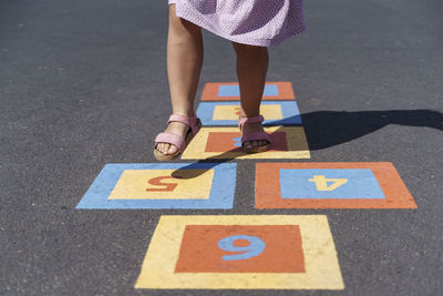 Girl playing hopscotch on footpath with numbers