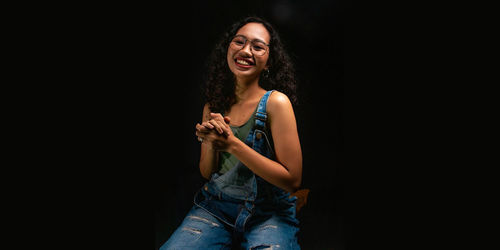 Portrait of smiling young woman against black background