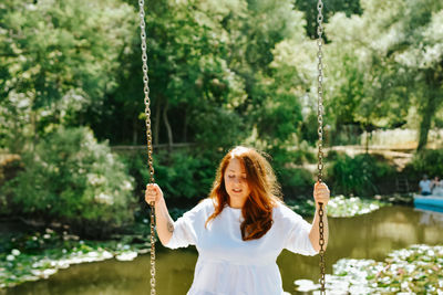 Rear view of young woman swinging against trees