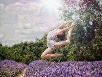 Woman jumping on lavender field against sky